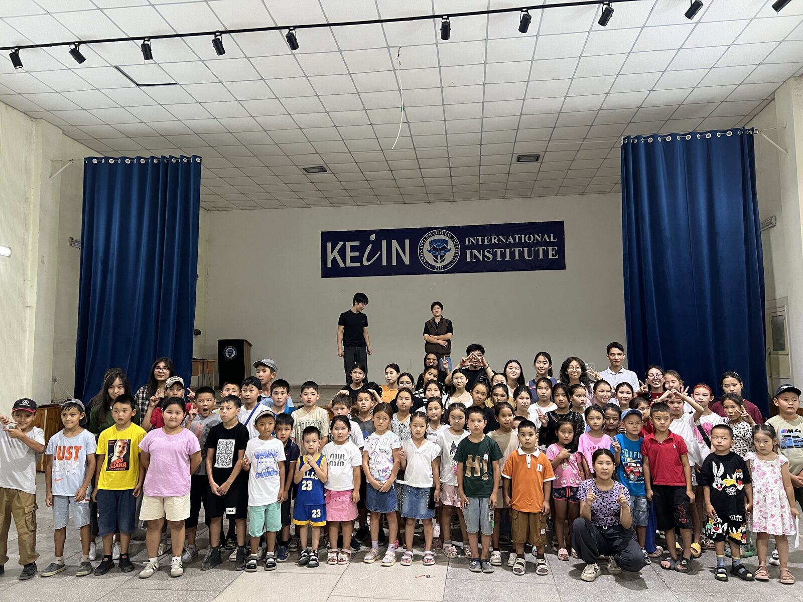 Large group photo of campers and mentors on stage at KEIIN International Institute