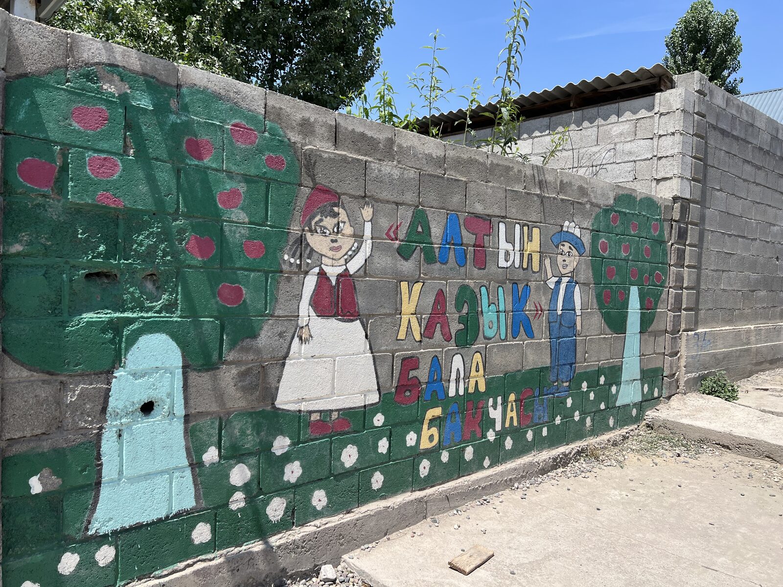 Mural reading Altyn-Kazyk Kindergarten, painted on a cinderblock wall with camp kids